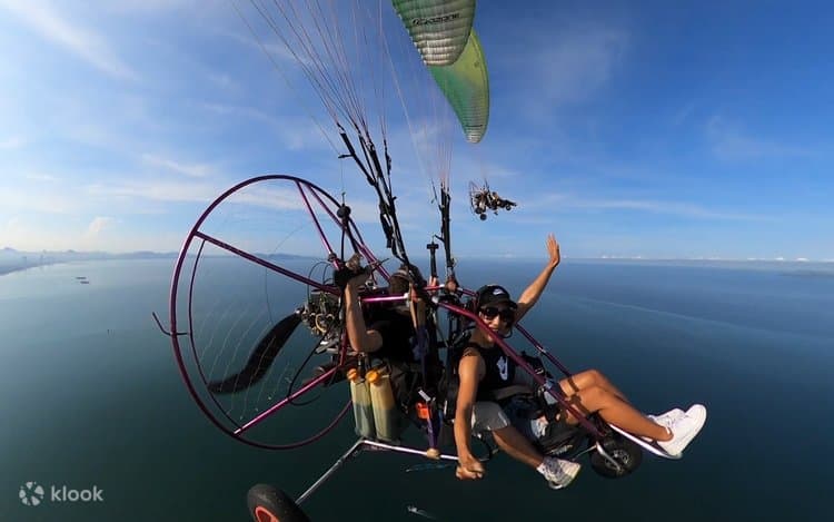 Tandem paramotor trike flying above the coast with its engine and propeller visible