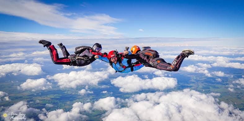 Tandem skydivers in freefall above clouds before parachute deployment